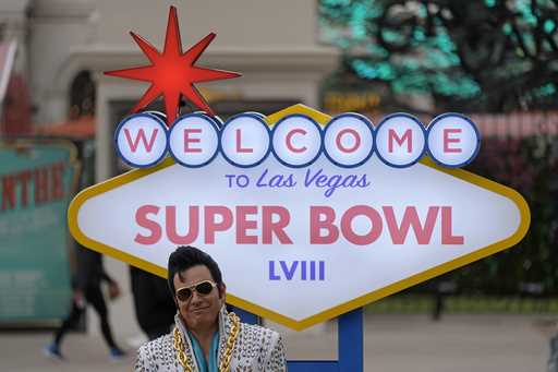 An Elvis impersonator waits to have his photo taken with visitors in front of a Super Bowl 58 sign …