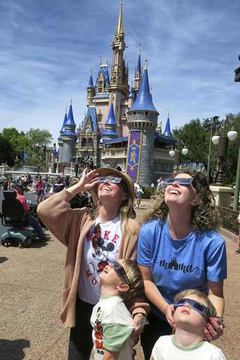 A family visiting from Sarasota watches the solar eclipse at the Magic Kingdom at Walt Disney World…