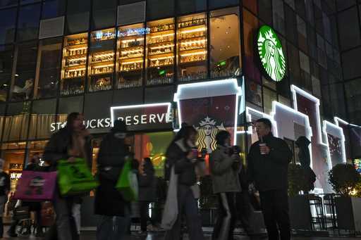 Shoppers walk by a Starbucks cafe at an outdoor shopping mall in Beijing on Saturday, December 23, …