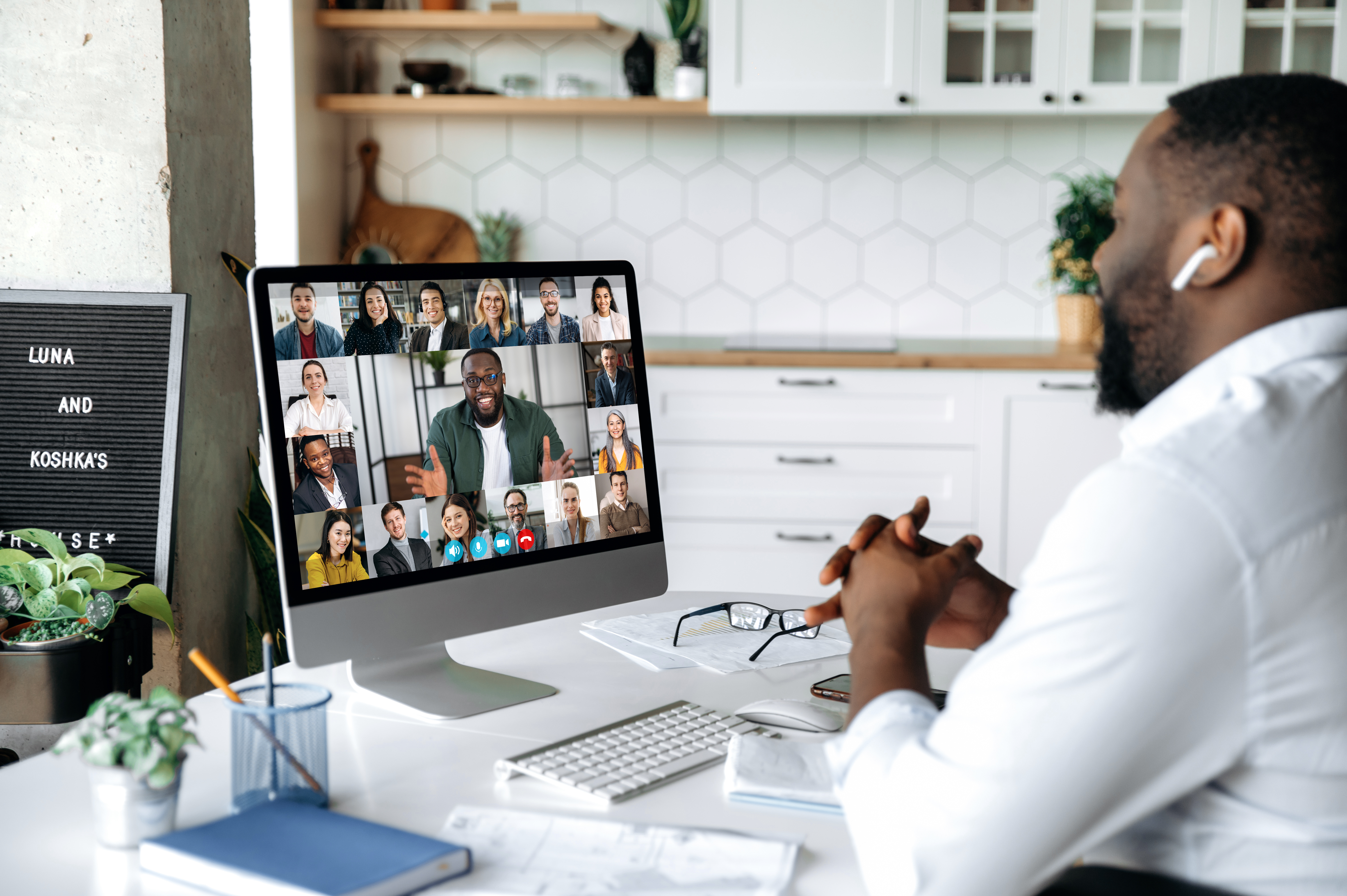man on zoom call with computer screen showing other teleconference attendees