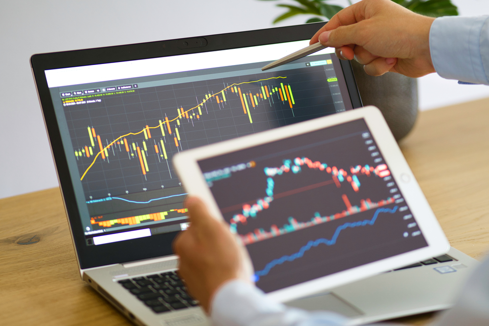 A male holding a tablet and comparing stock market statistics