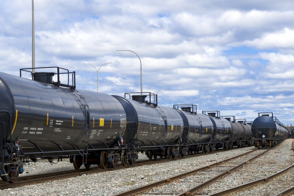 Black railway tanker cars of the type used to transport petroleum products. Several cars visible on two separate sets of tracks. Identification markings have been removed, only technical infomation remains.