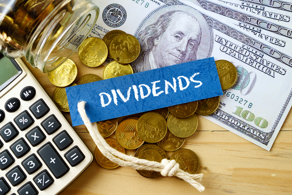 Finance conceptual image with DIVIDENDS words, hundred dollar bills, golden coins and calculator on wooden background.