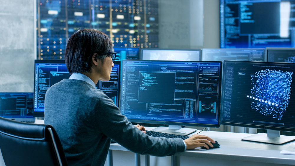 In the System Control Room Technical Operator Works at His Workstation with Multiple Displays Showing Graphics