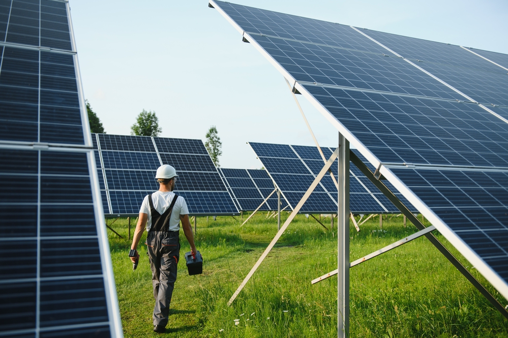 Male worker in uniform outdoors with solar batteries at sunny day