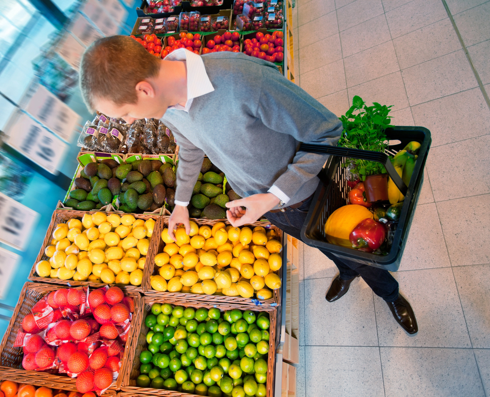 Photo of man in grocery store picking fruit to put in a basket that contains a variety of fruit. Representative of a basket of stocks, like mutal or index funds.