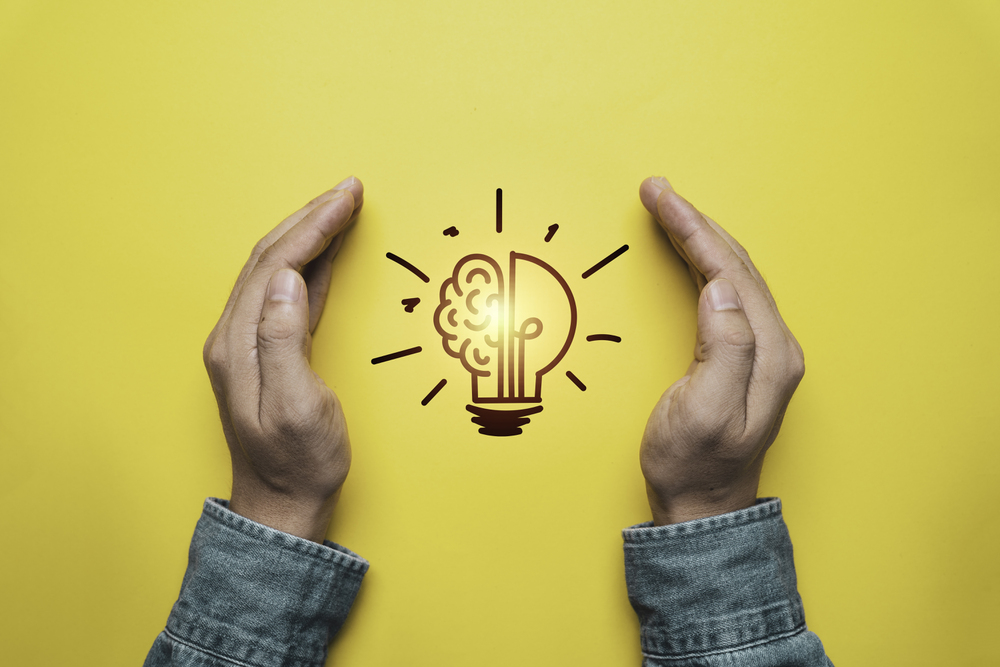Photo of two hands cupping a glowing lightbulb on yellow background