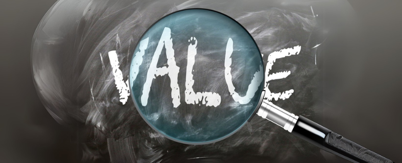 Photo of the word VALUE written on a black chalkboard with a magnifying glass over the word.