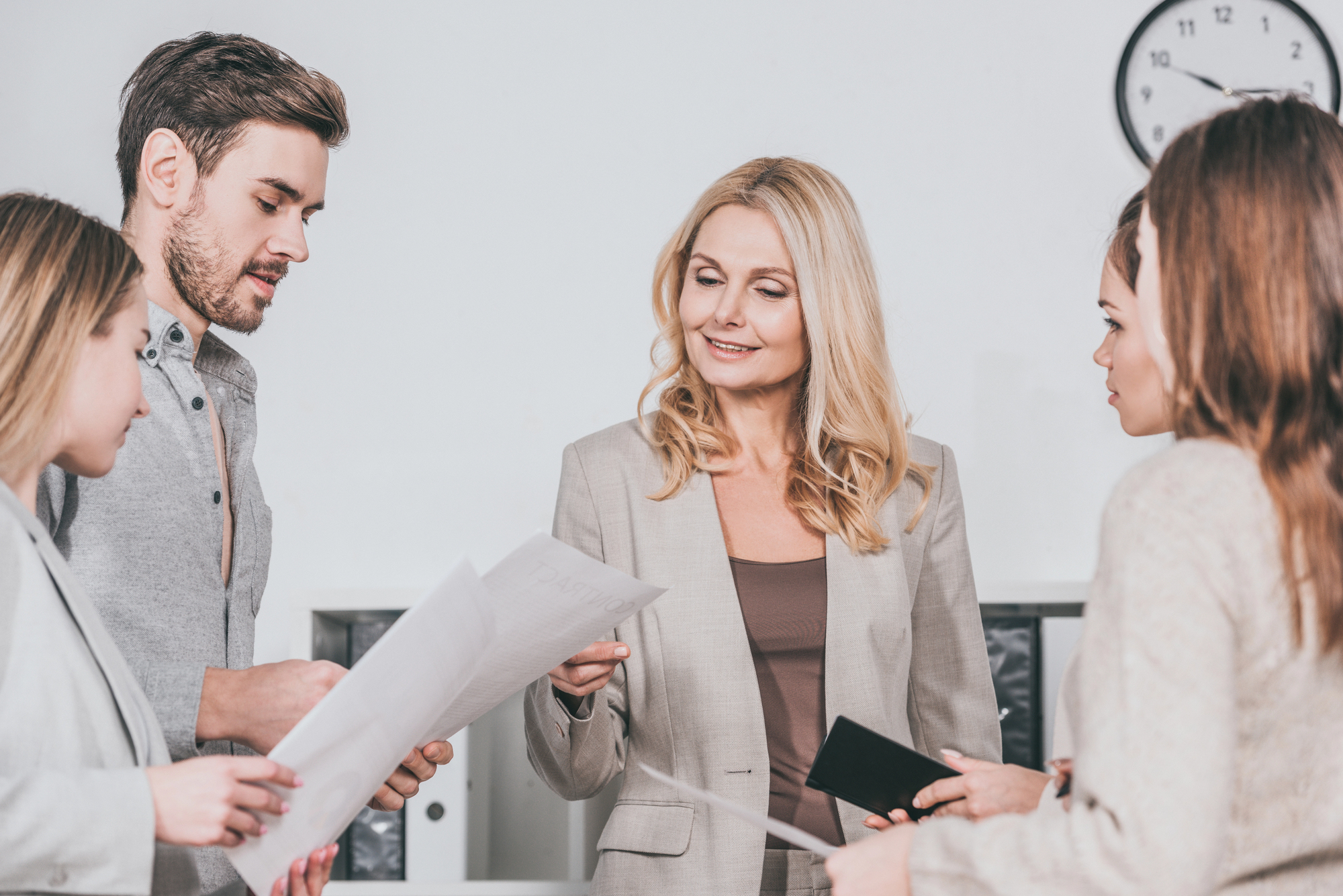 Smiling professional female business mentor looking at papers and working with young colleagues in office