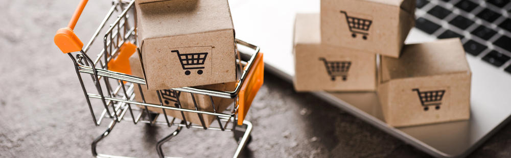 Panoramic shot of toy shopping cart with small carton boxes near laptop, e-commerce concept — Photo