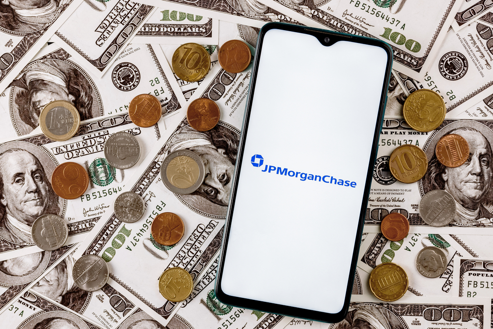 Kazan, Russia - Nov 24, 2021: Smartphone with JPMorgan Chase bank logo surrounded by variety of metal coins on background of dollar bills — Stock Editorial Photography