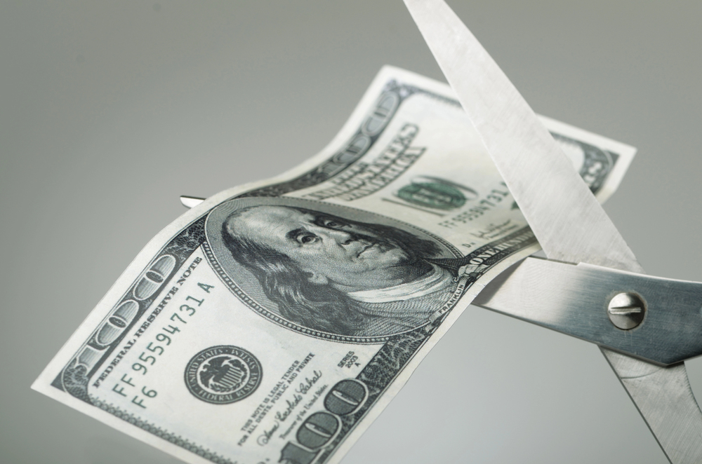 Scissors cutting $100 bill in half