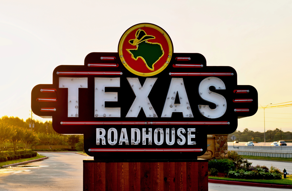Texas Roadhouse restaurant sign on the side of a freeway in Humble, Texas during an early morning sunrise.