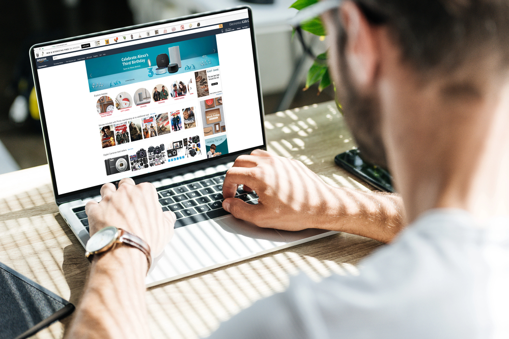 Back view of man using laptop with amazon website on screen - Stock Editorial Photography