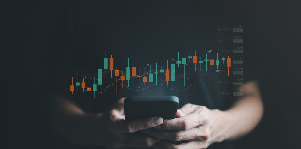 A businessman looking at stock information on smartphone with stock chart overlay