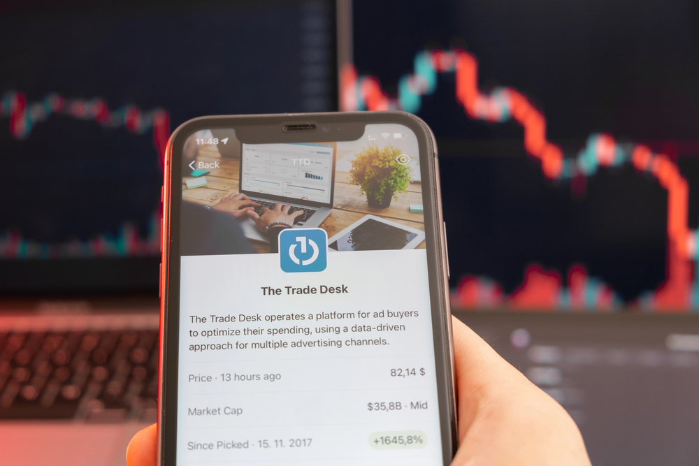 The Trade Desk stock price downtrend with red graphs on the background. Man hands holding a smartphone with logo on the screen, February 2022, San Francisco, USA — Stock Editorial Photography