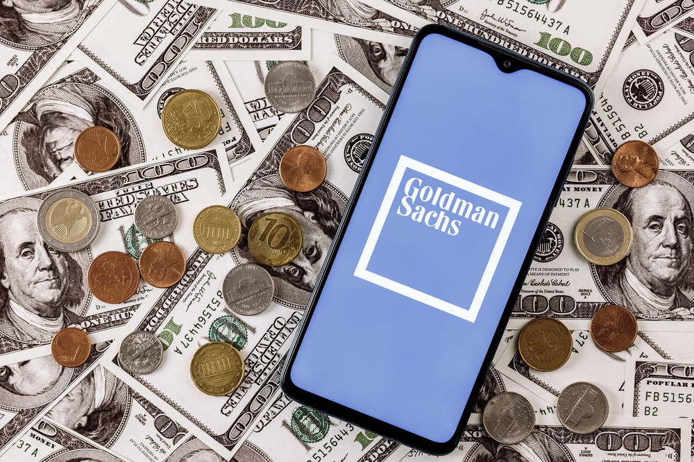 Kazan, Russia - Dec 20, 2021: Smartphone with Goldman Sachs bank logo surrounded by variety of metal coins on background of dollar bills — Stock Editorial Photography