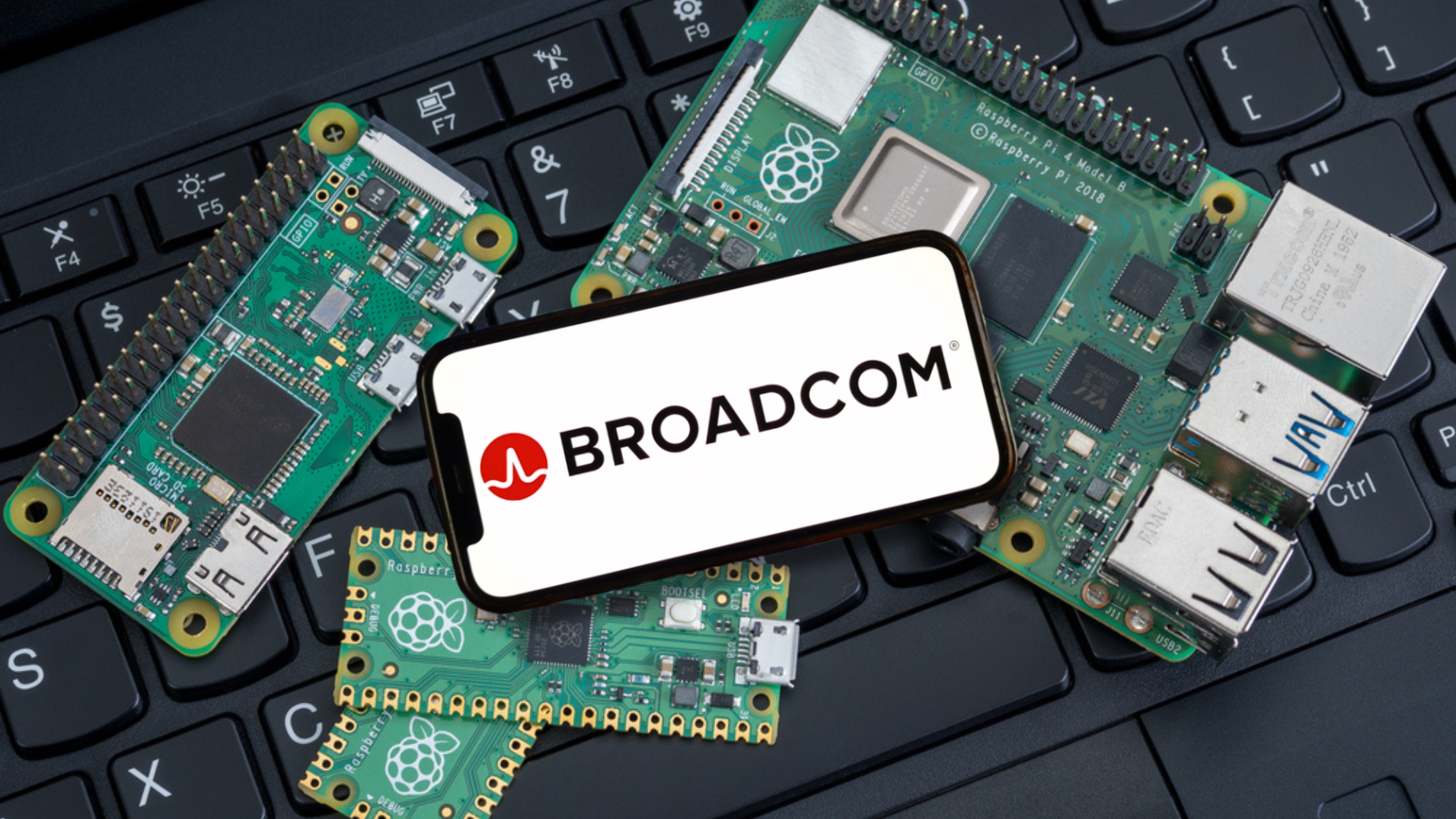 Broadcom logo on cellphone with chip boards on keyboard - This image is an original composition by MarketBeat using licensed and editorial elements. Not for redistribution or reuse.