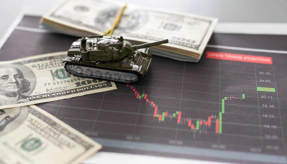 A toy tank, dollars on top of a tablet showing a stock chart.
