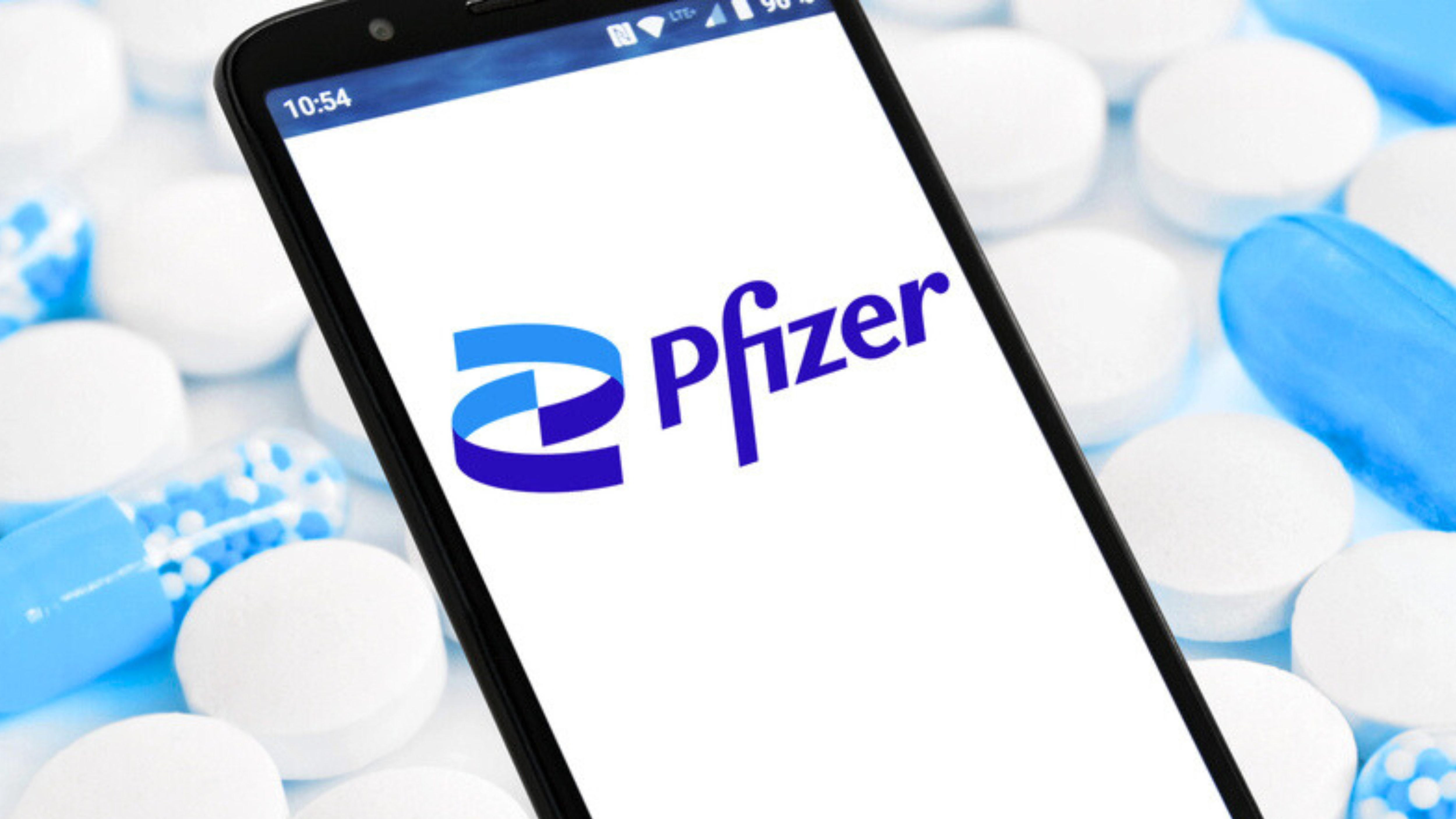 Smartphone with Pfizer Logo against blue tablets and capsules Background — Stock Editorial Photography