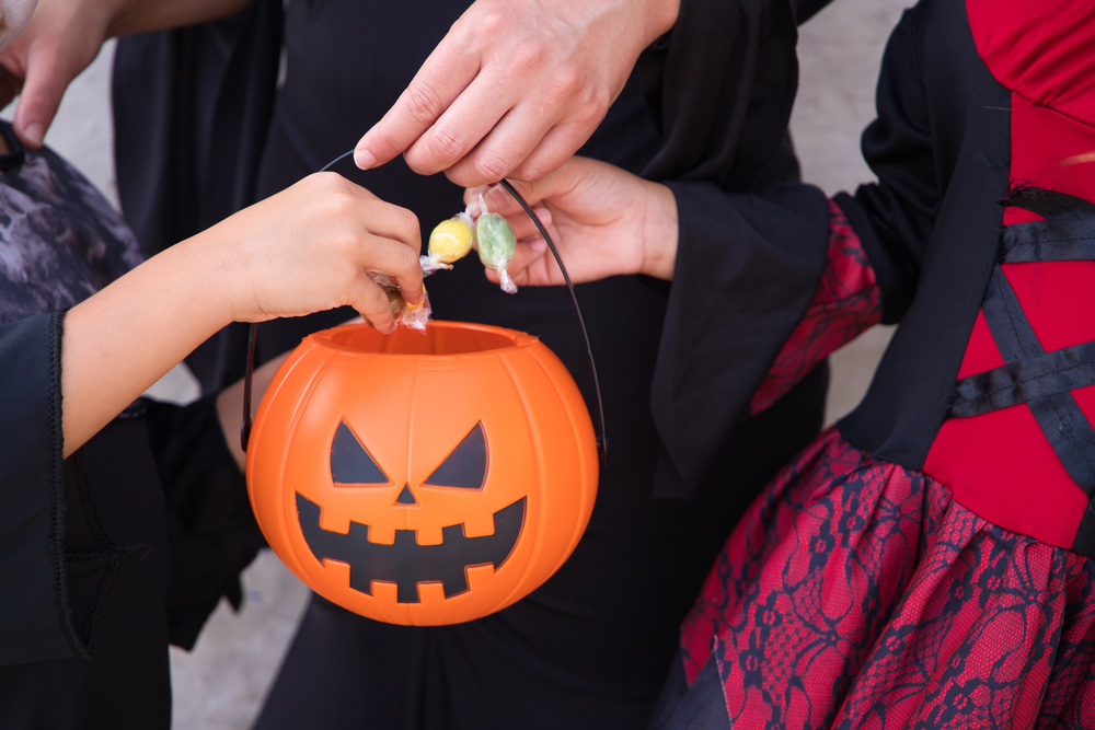 details of hands of woman, boy and girl putting candy and sweets in a halloween pumpkin. trick or treat.