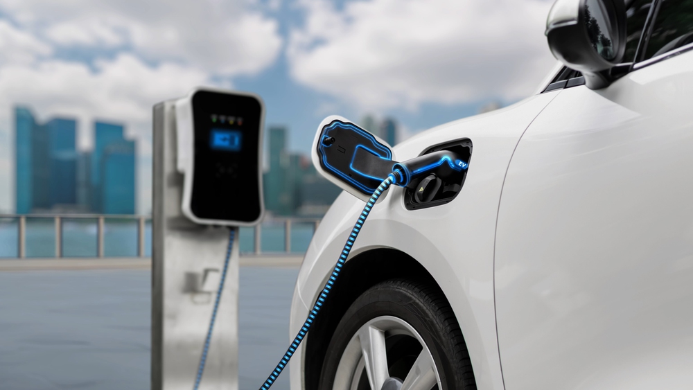 Electric car plugged in with charging station to recharge battery with electricity by EV charger cable with city background. Future innovative ev car and energy sustainability. Peruse