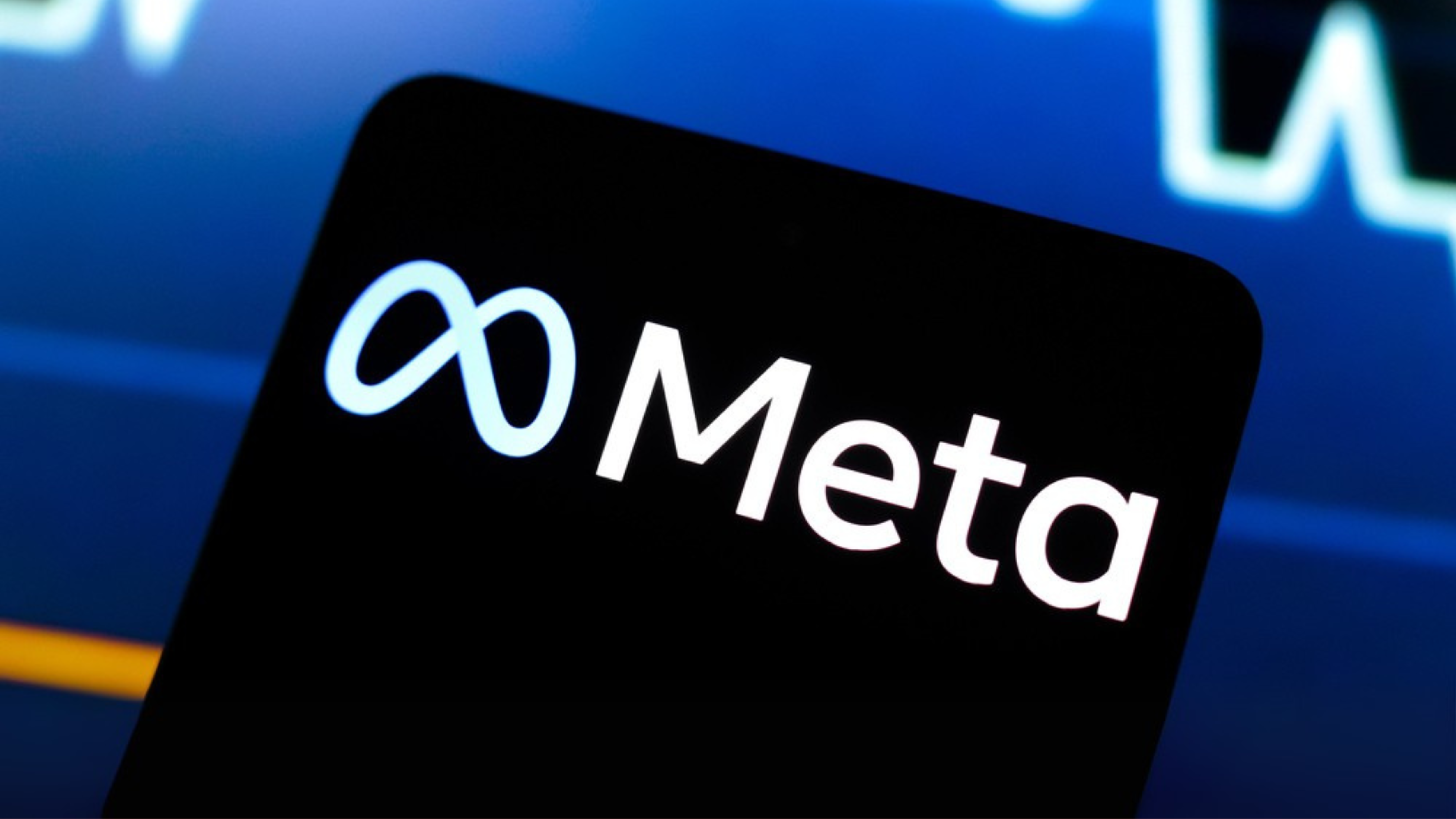 Meta logo is displayed on a smartphone screen and in the background, a stock market graph