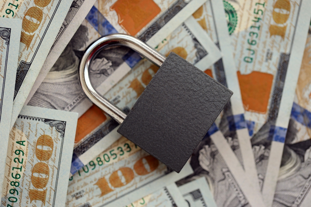 Small black padlock lies on big amount of new hundred US dollar bills close up