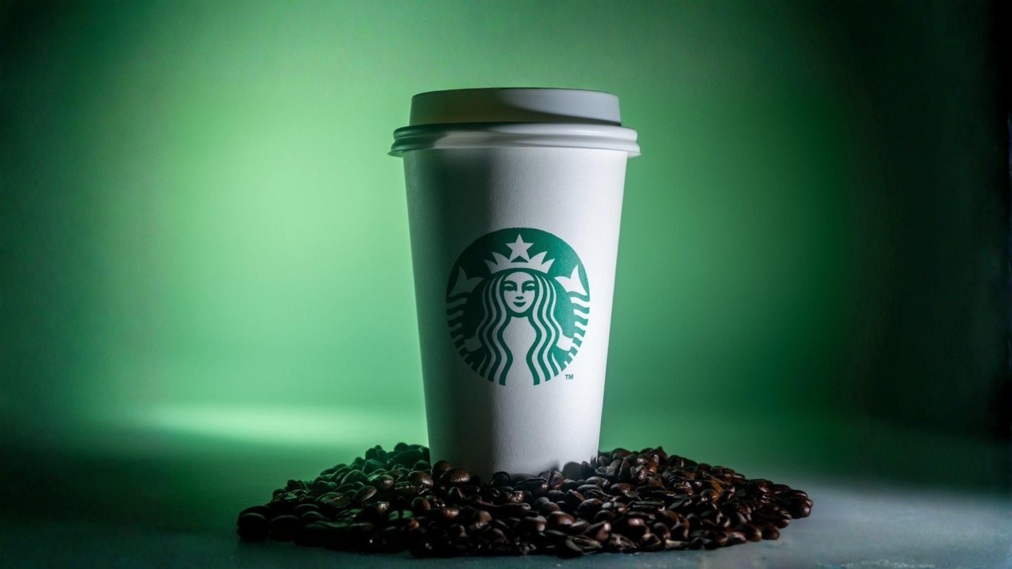 Starbucks white cup with logo on top of coffee beans, green background