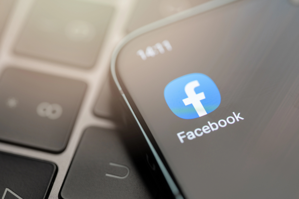 Facebook app on smartphone screen against laptop keyboard in background. 