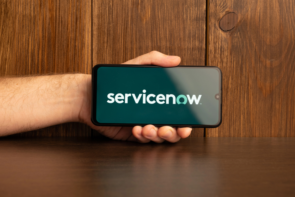 Servicenow logo on a smartphone near modern laptop on wooden background.