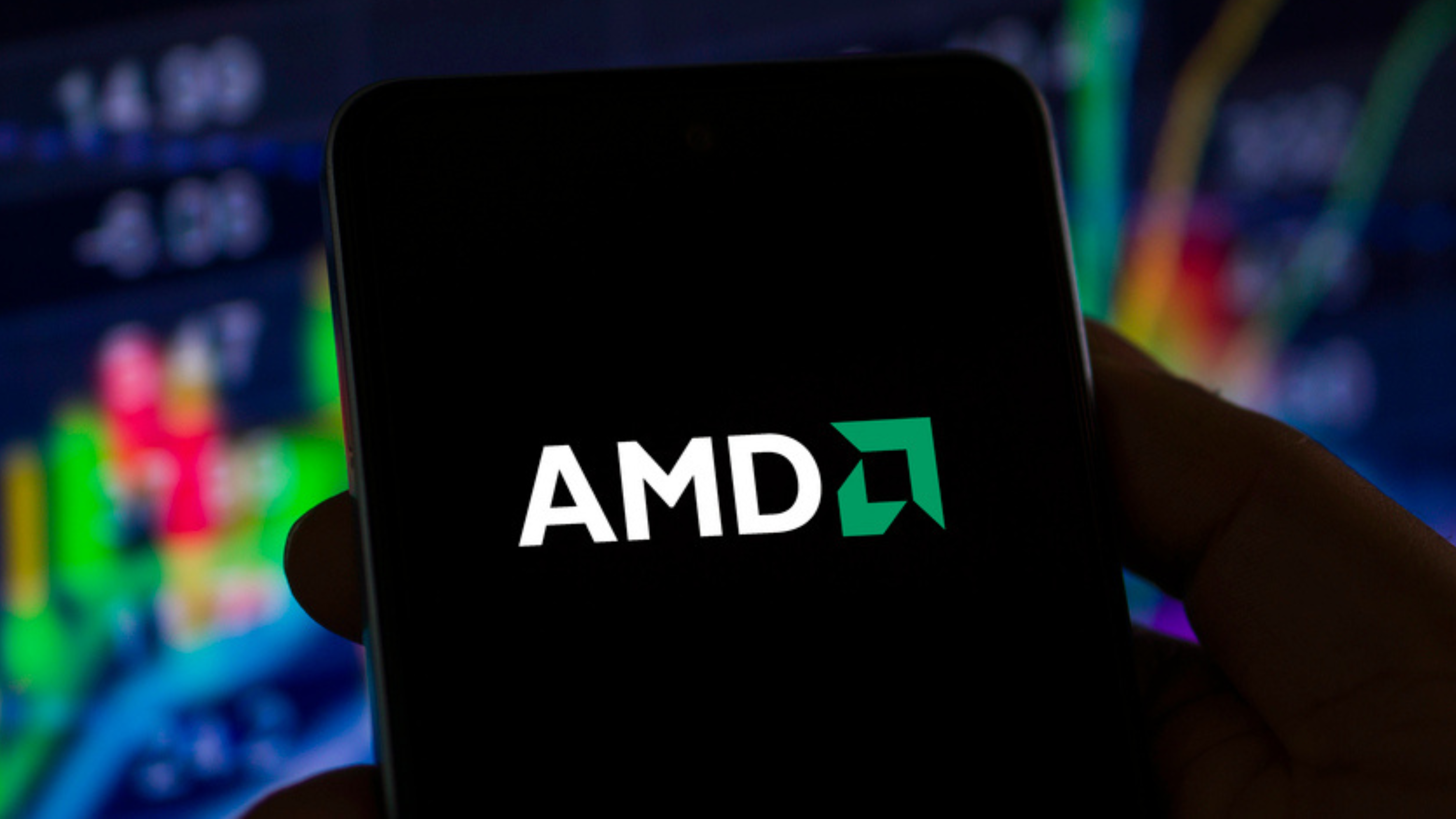 Hand holding mobile phone with AMD logo, stock chart in background.