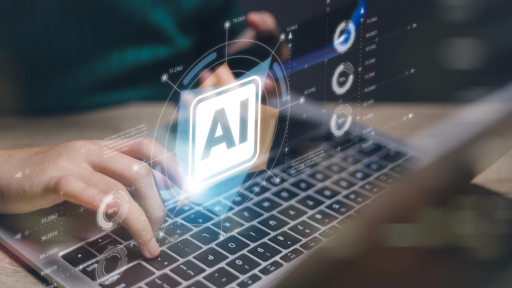 A person is typing on a laptop with a blue screen that says AI.