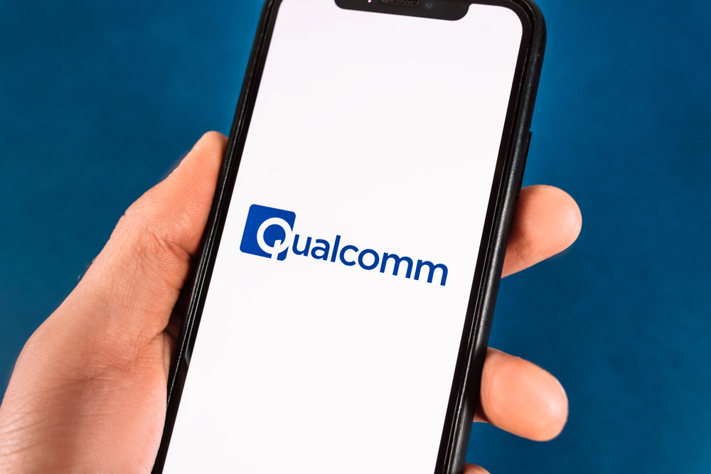 Hand holds smartphone with Qualcomm logo.