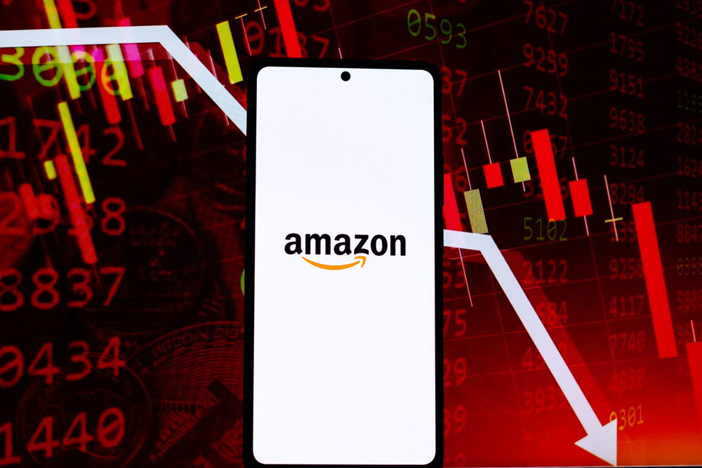 Amazon logo on phone screen with dropping stock chart in the background.