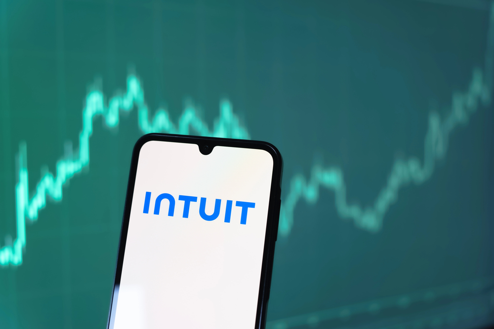 Intuit logo on smartphone, with rising stock chart in background.