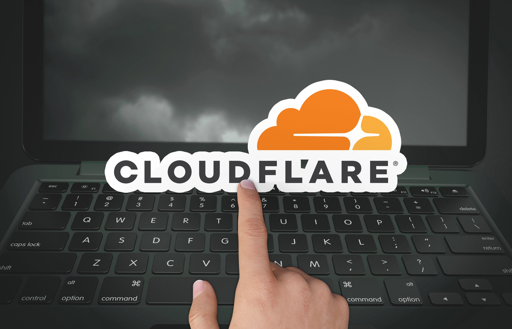 Finger pointing to Cloudflare logo in front of laptop computer.