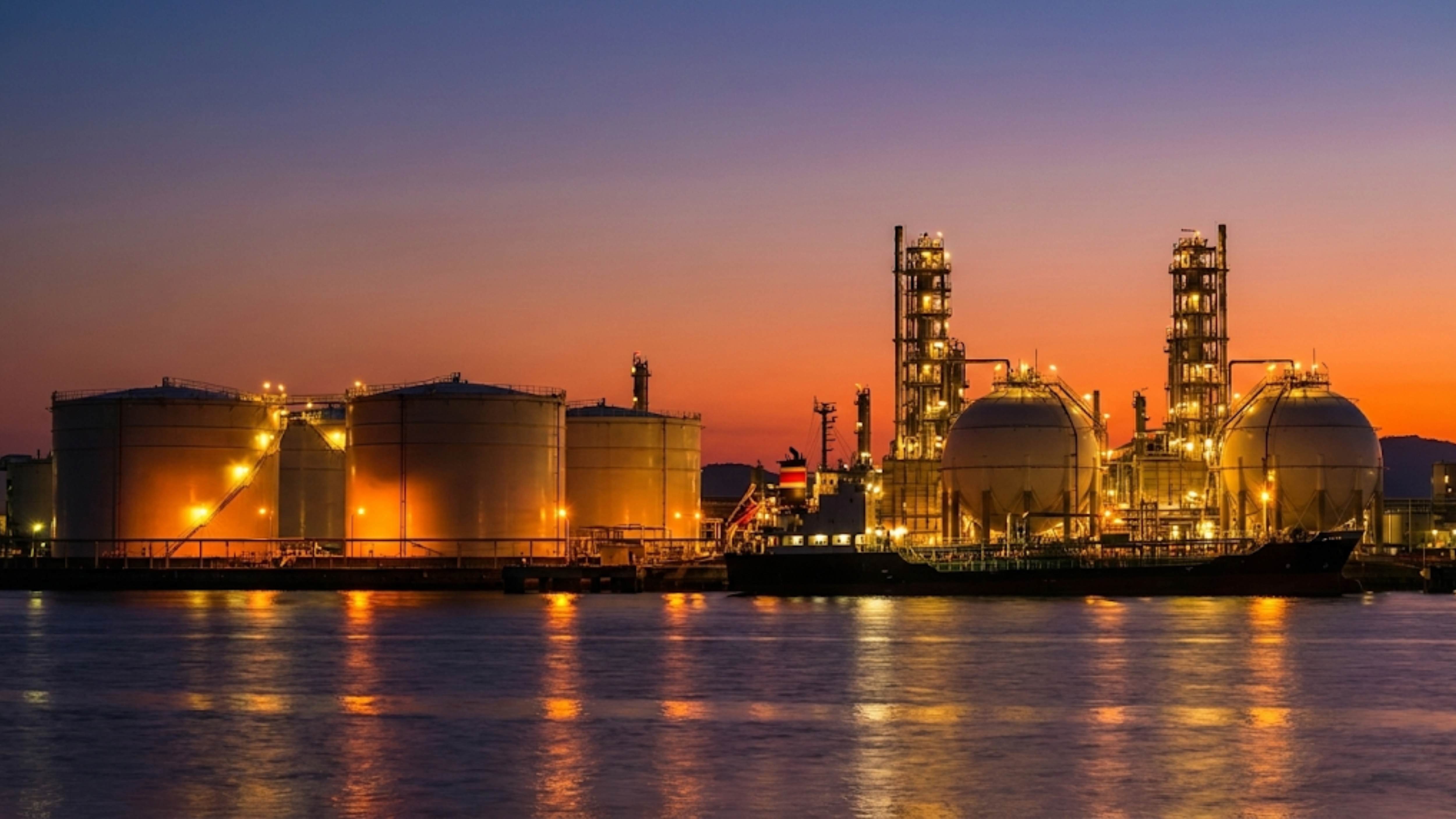 Oil and gas storage tanks glow at sunset highlighting energy infrastructure tied to fuel supply and commodity markets.