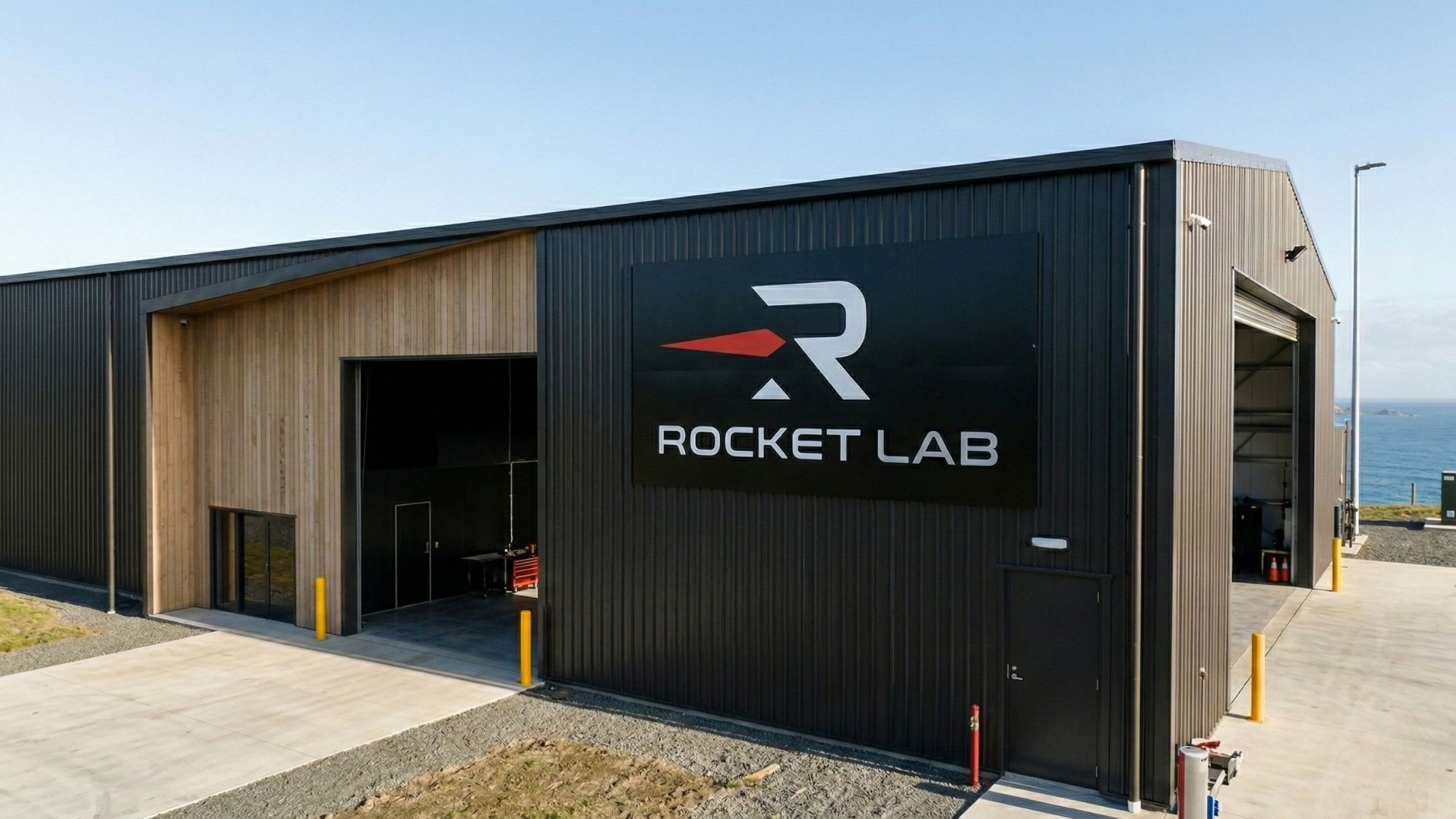 Imaginative depiction of a Rocket Lab facility with company logo on modern industrial building near coastline