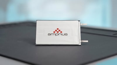 Amprius lithium battery pouch cell with the company logo on a silver casing resting on a dark surface in a lab setting.