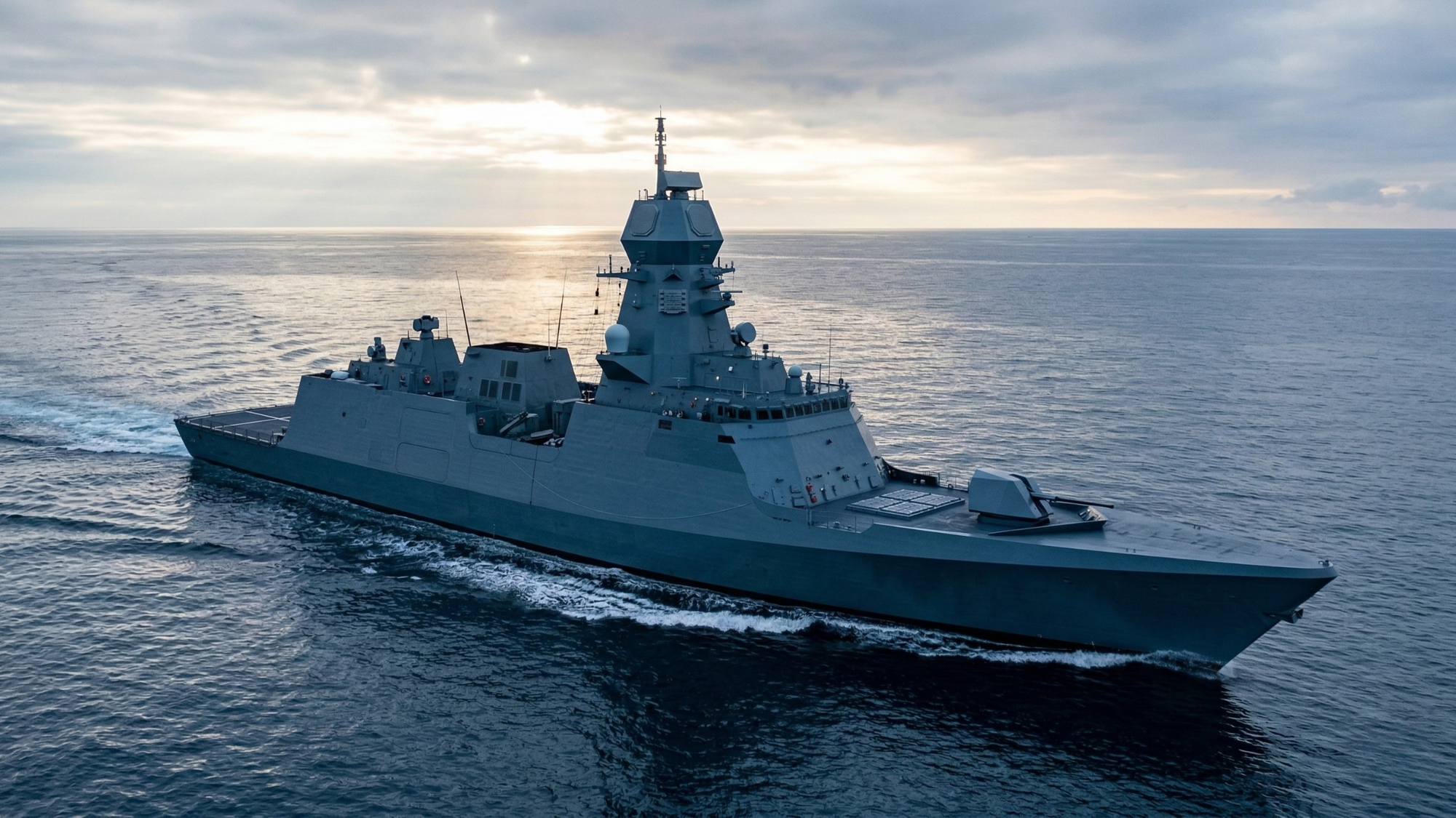Modern naval warship cruising across open ocean waters at sunrise, viewed from above, showcasing advanced defense technology and military maritime power.