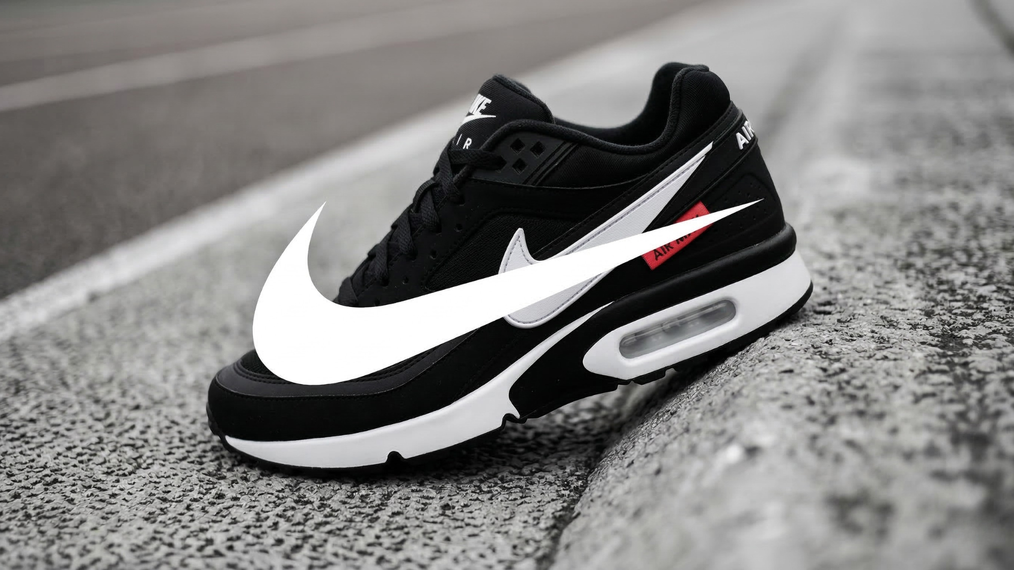 Black Nike Air sneaker with a large white swoosh resting on asphalt pavement, representing Nike’s athletic footwear brand.