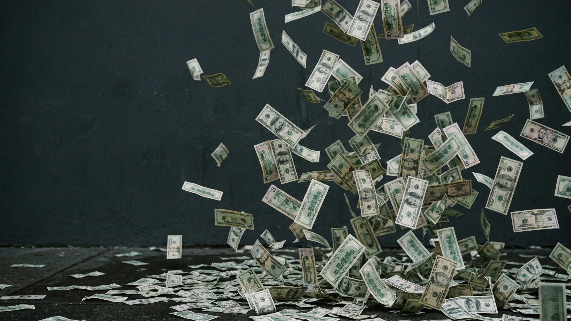 Falling US dollar bills scattered across a dark surface, symbolizing rising dividends and strong shareholder returns in financial markets.