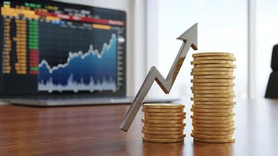 An upward arrow between two stacked coin piles on a desk, with a rising stock price chart on a laptop screen behind.
