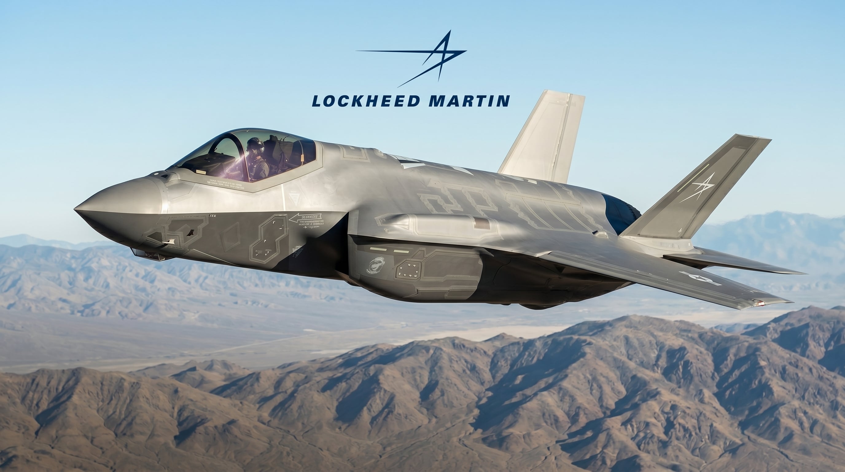 A Lockheed Martin F-35 fighter jet flies over a mountainous landscape with the company logo visible.