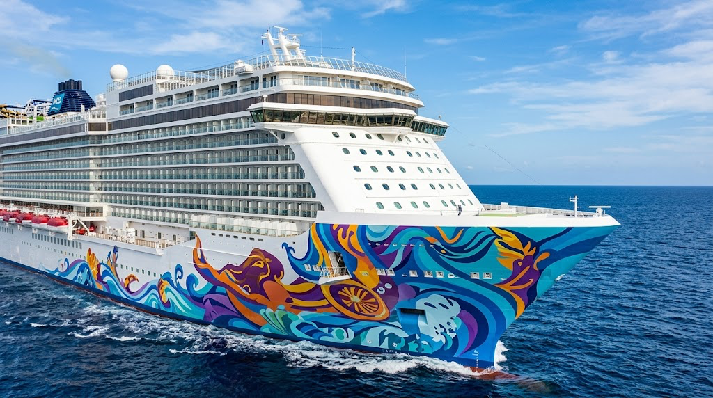 A Norwegian Cruise Line ship with colorful hull artwork sails on open ocean under blue skies.
