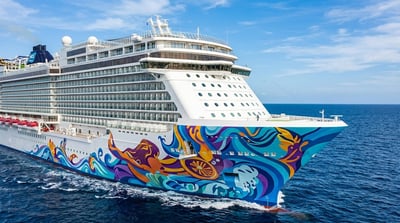 A Norwegian Cruise Line ship with colorful hull artwork sails on open ocean under blue skies.