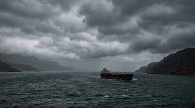 A cargo tanker ship navigates choppy open waters under a dark, overcast sky near rocky coastlines.