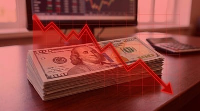 A stack of U.S. hundred-dollar bills on a desk overlaid with a red downward-trending stock chart.