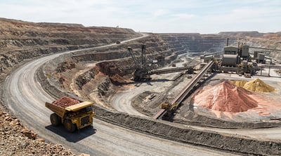 An aerial view of a large open-pit mine with a haul truck, conveyor belts, and ore stockpiles.